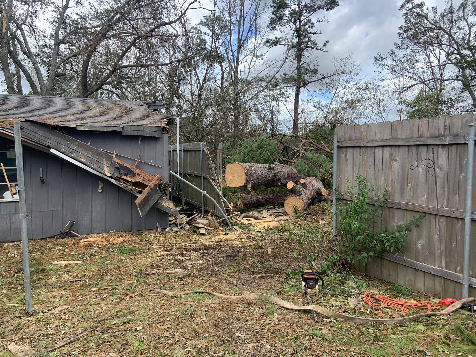 A house with a roof that has fallen down and a pile of logs in front of it.
