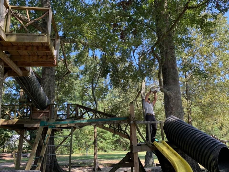 A man is standing on top of a wooden playground with a slide.