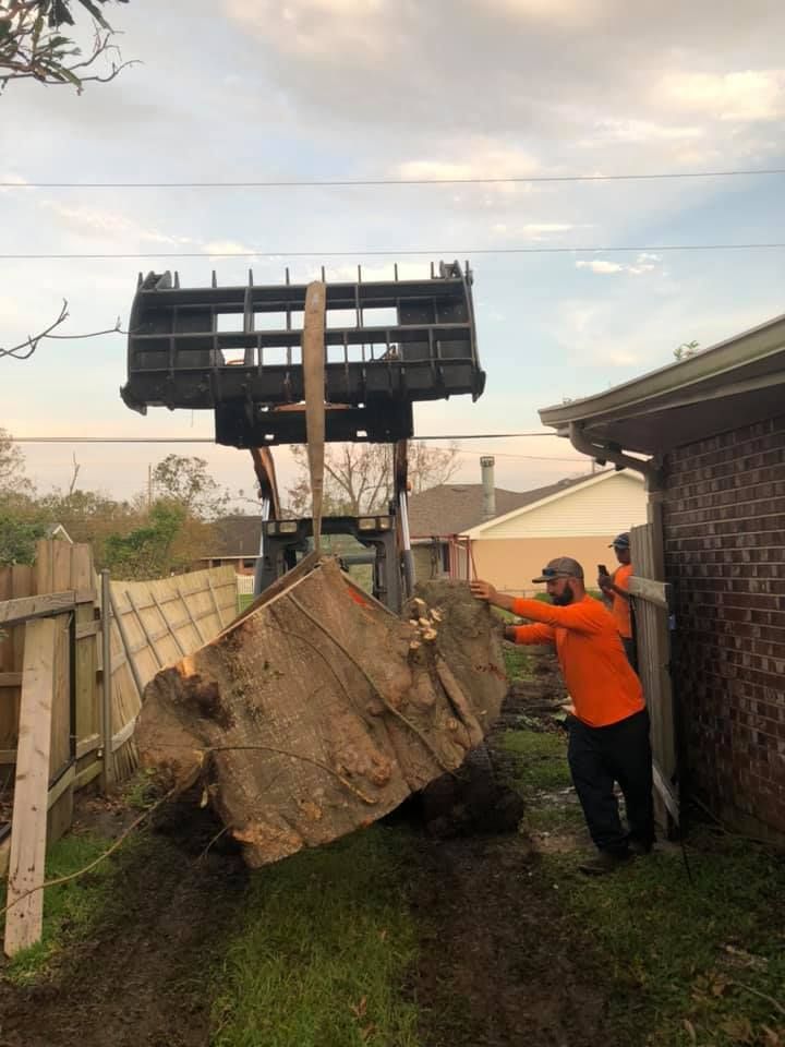 A man is standing next to a tractor that is lifting a large rock.
