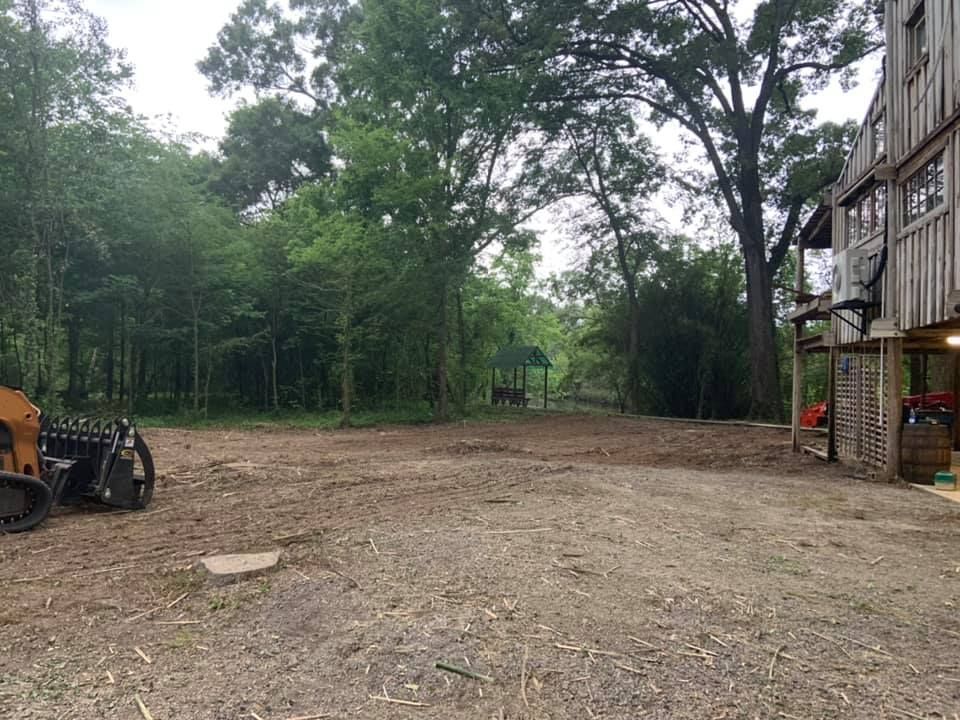 A large dirt field with trees in the background and a house in the background.