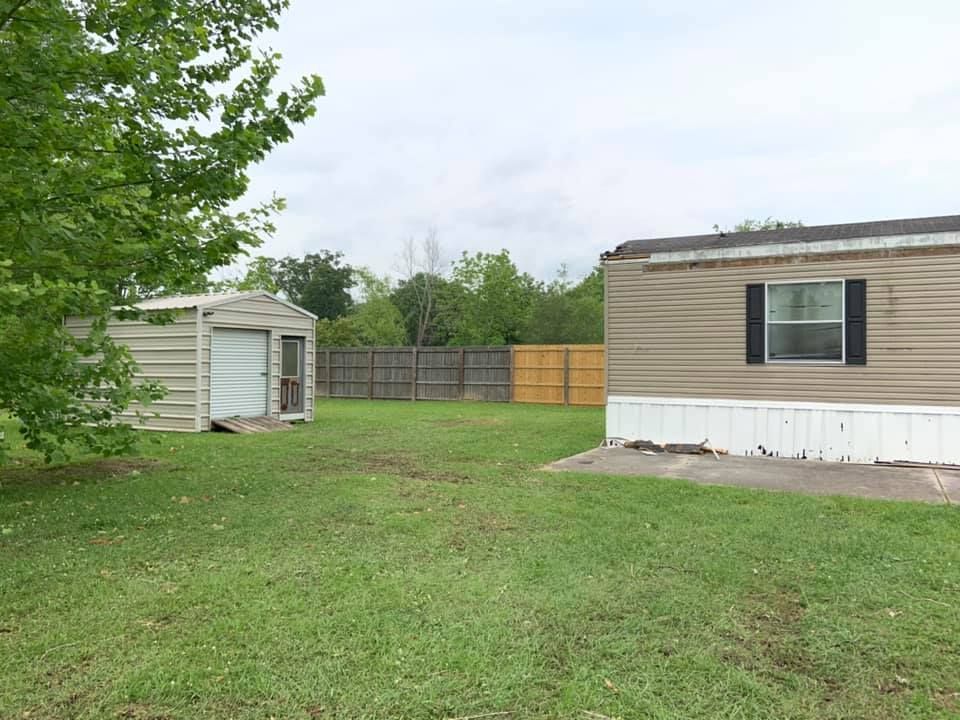 A mobile home is sitting in a grassy yard next to a shed.