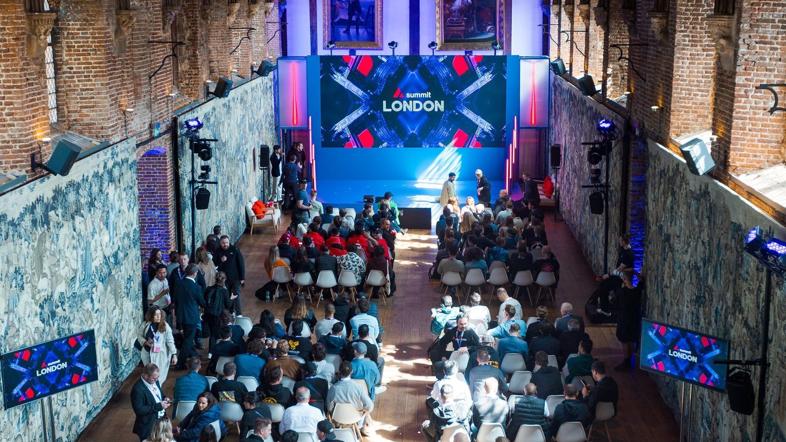 A high-angle view of a presentation in a brick-walled hall with a large screen displaying "League of Legends" branding.
