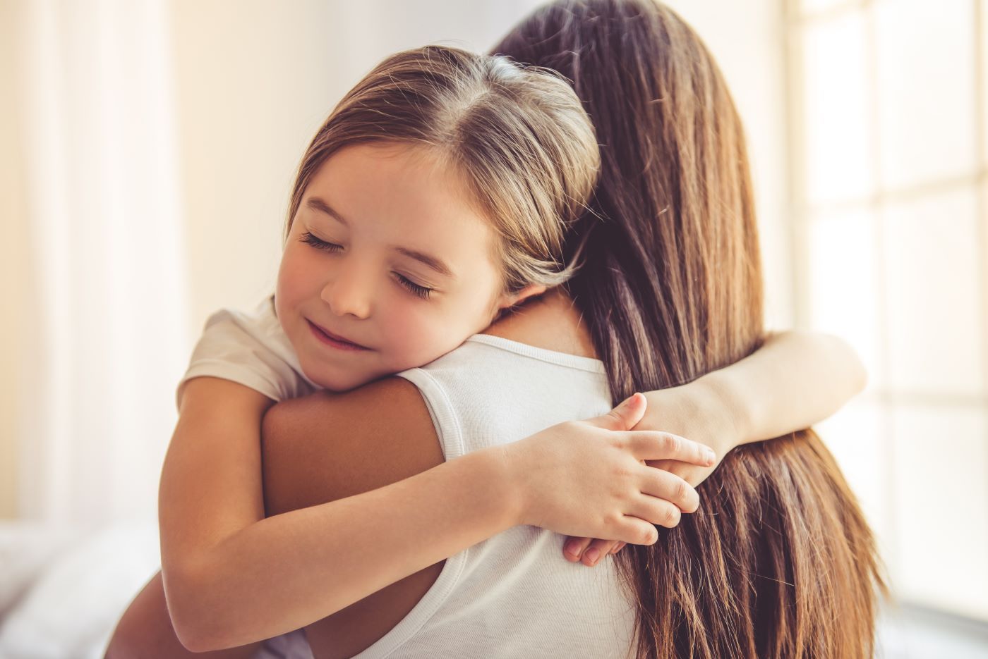 A little girl is hugging her mother on a bed.