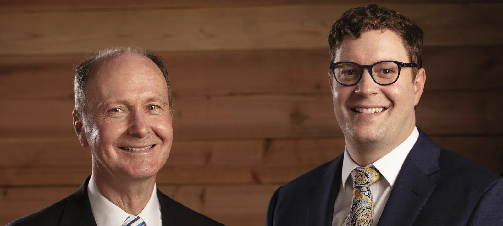 Two men in suits and ties are standing next to each other and smiling.