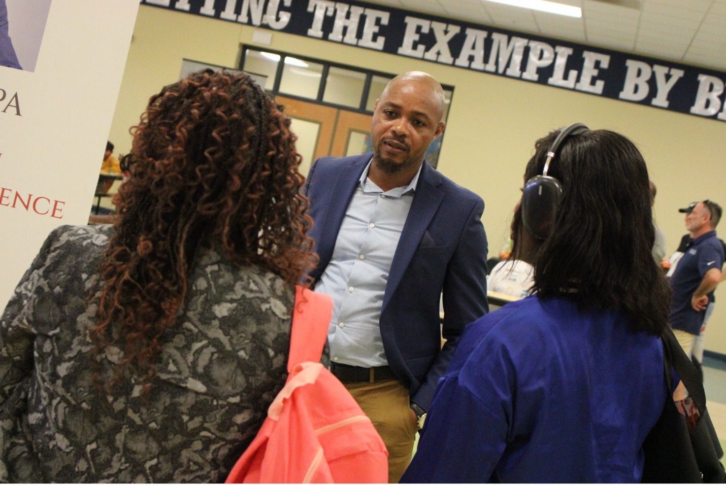 Man in suit conversing with two women in a hallway.