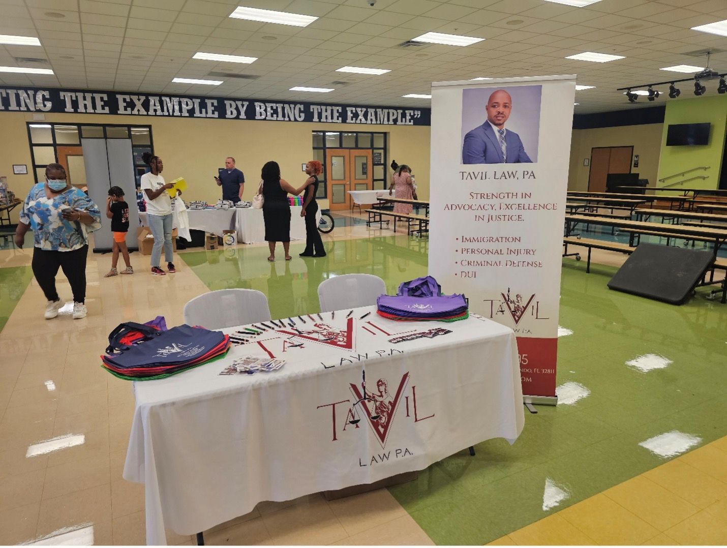 Event with table, banner featuring a man, people in a school cafeteria.