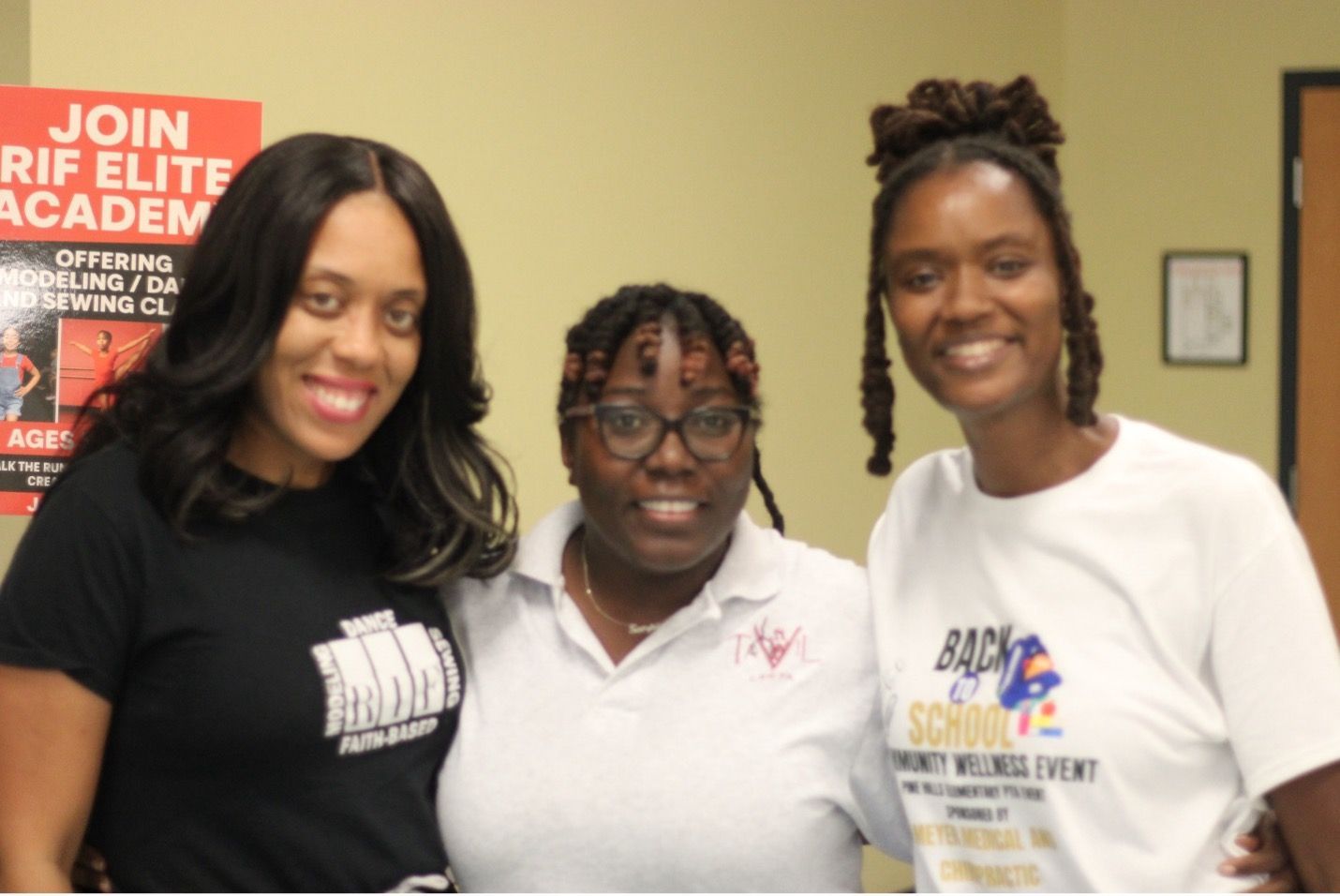Three women smiling, posing for a photo at a back-to-school community event.