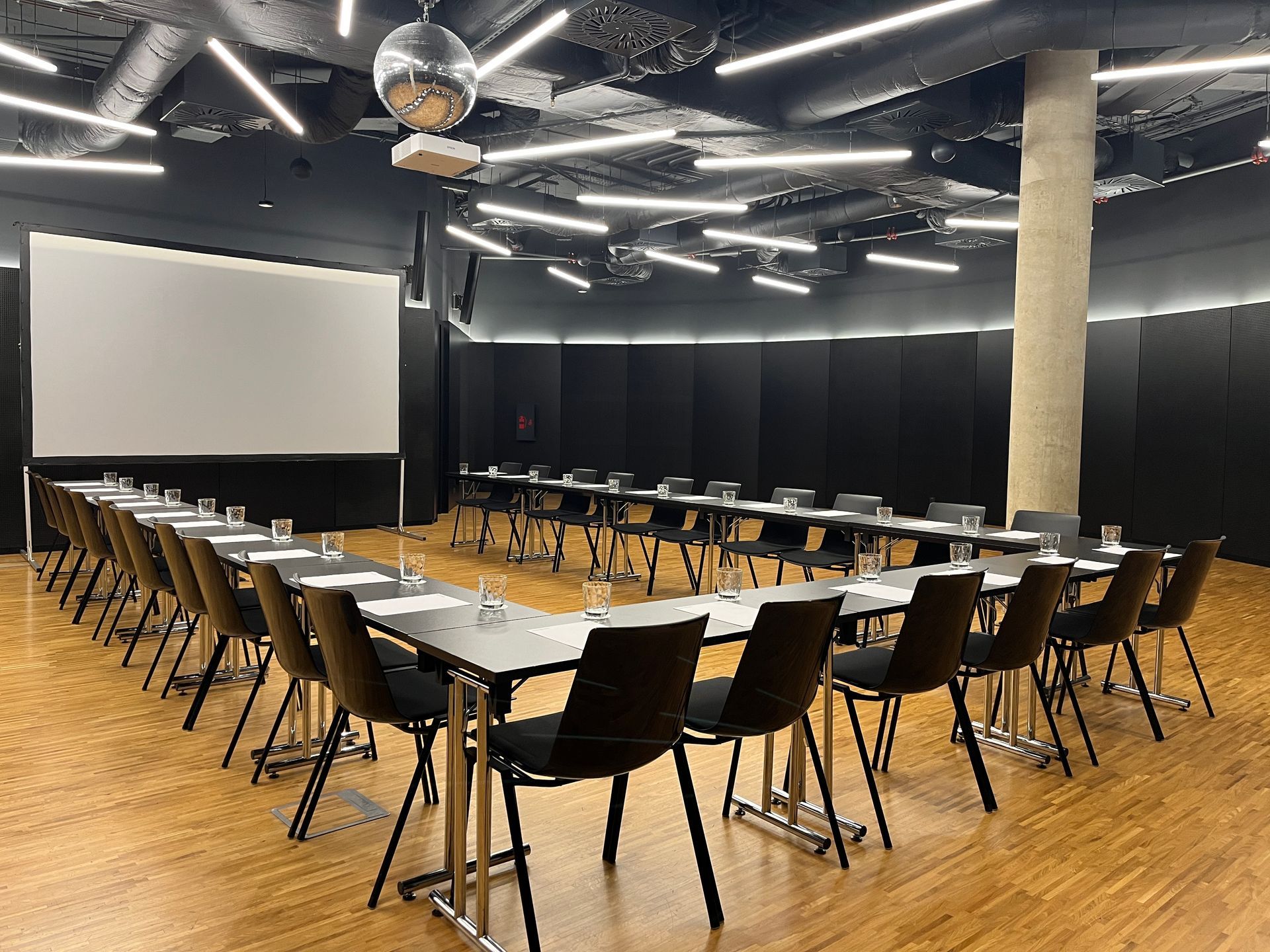 Konferenční místnost se stoly a židlemi a velkou obrazovkou.