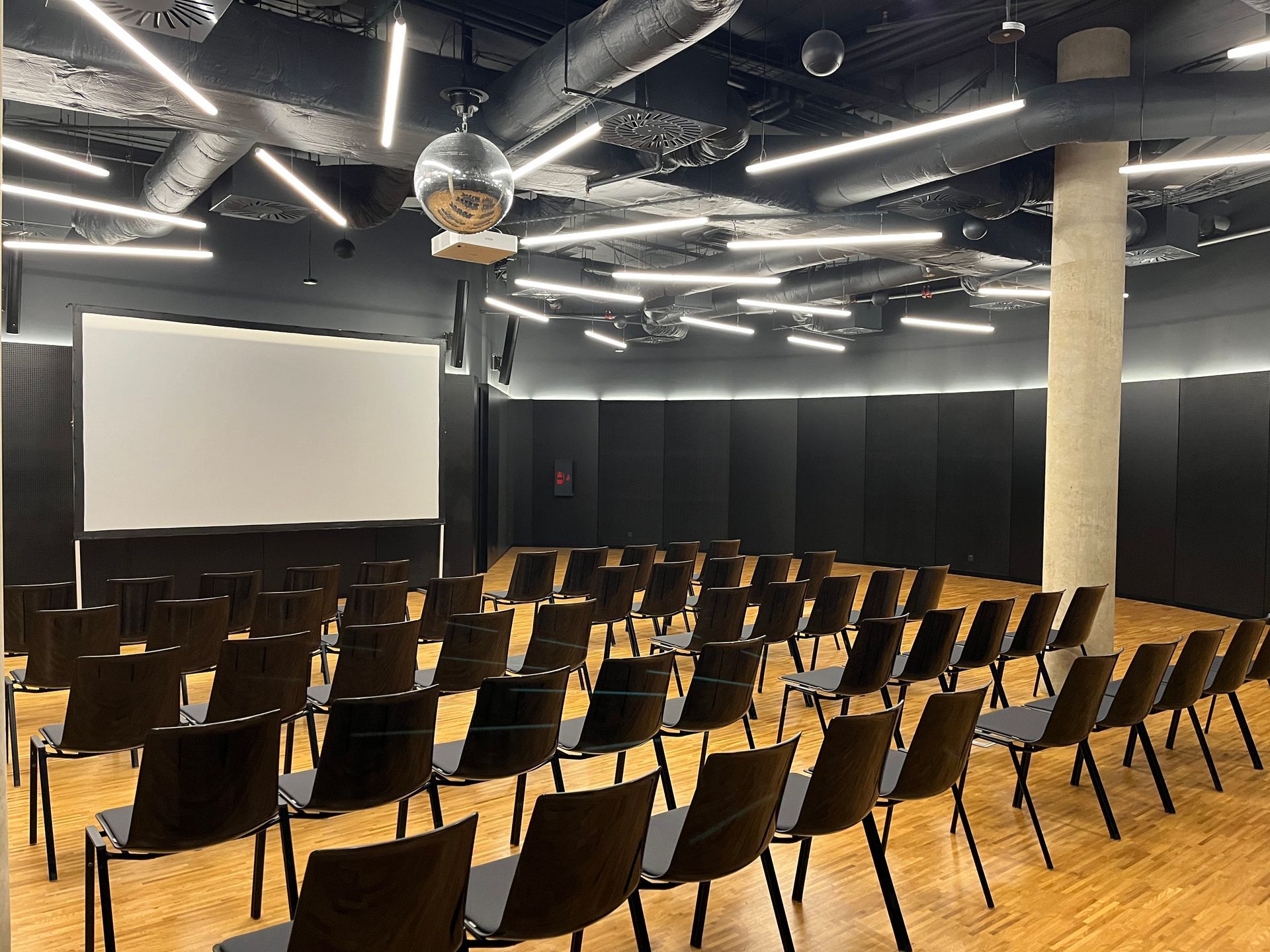 Velká místnost s řadami židlí a promítacím plátnem.