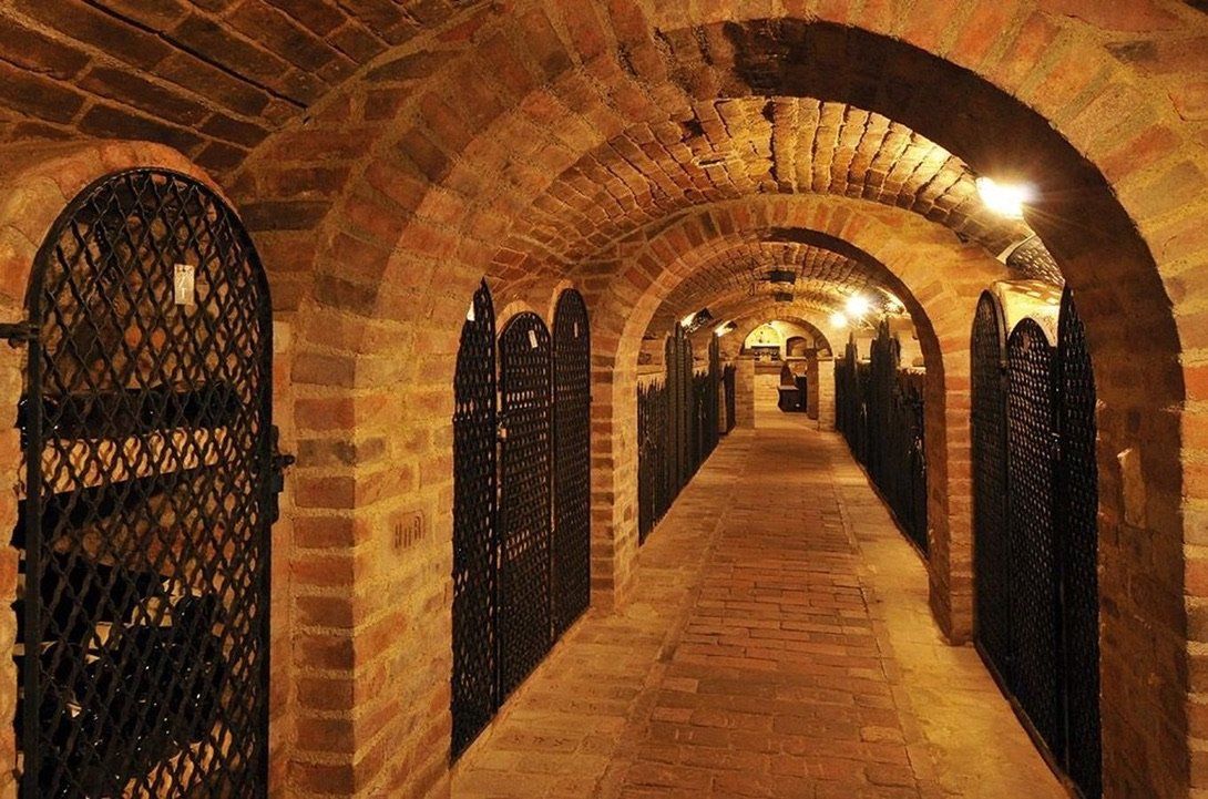 Dlouhý cihlový tunel s kovovými vraty vedoucí do vinného sklepa.