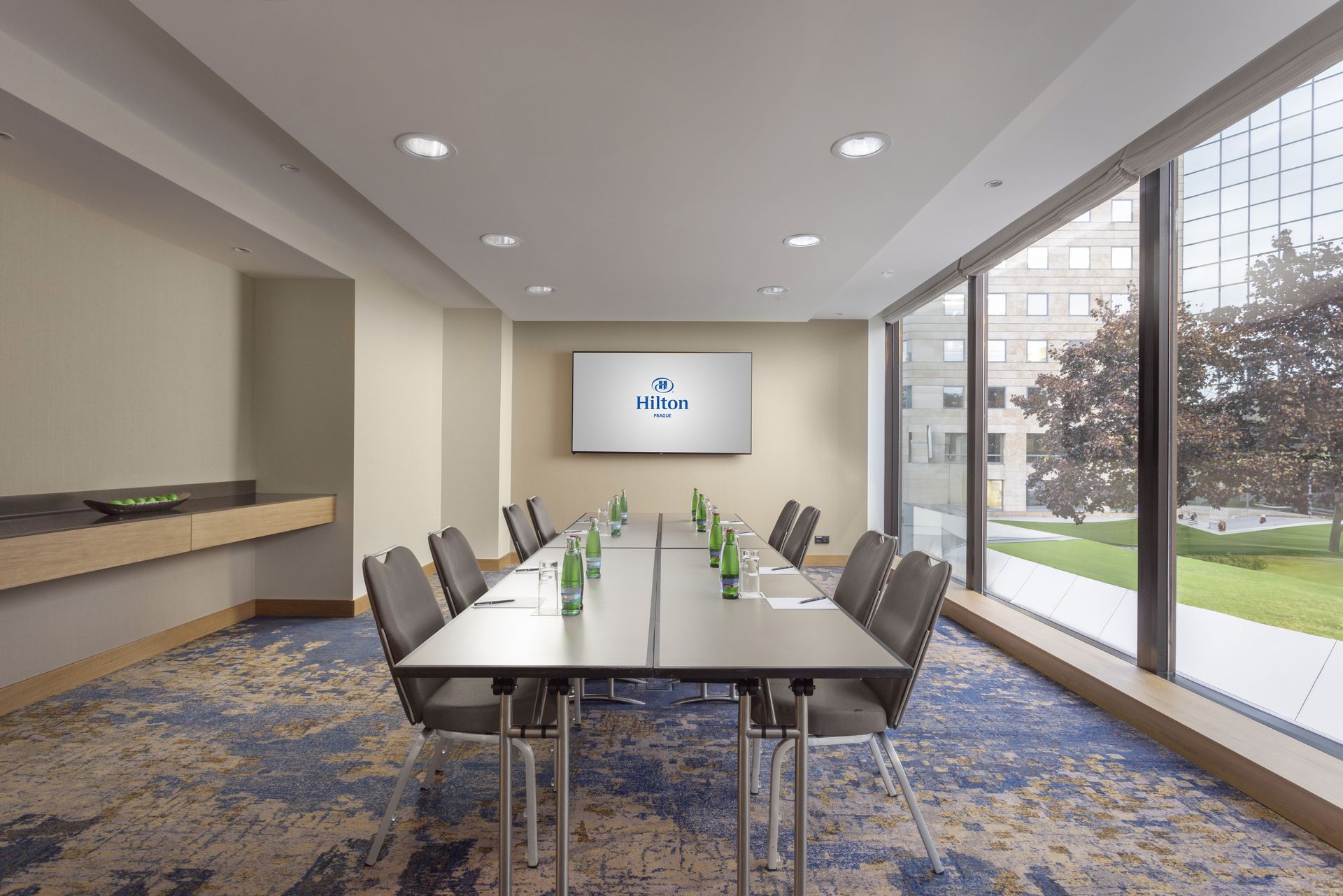 Konferenční místnost s dlouhým stolem a židlemi a TV s plochou obrazovkou.