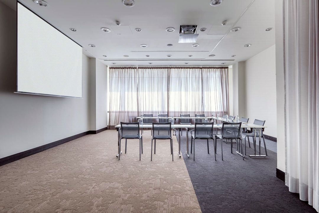 Konferenční místnost se stoly a židlemi a velkou obrazovkou.