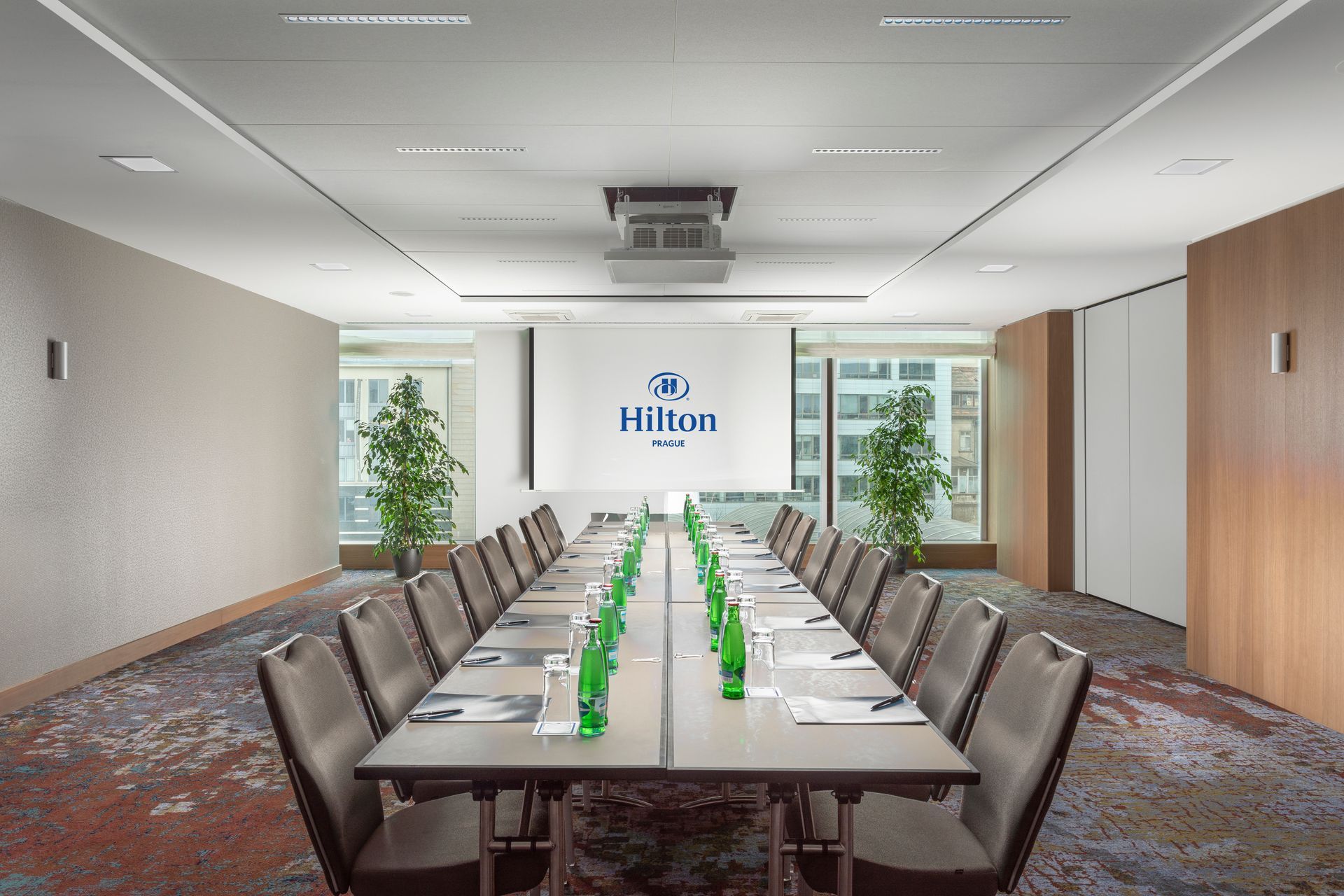 Konferenční místnost se stoly a židlemi a velkou obrazovkou.