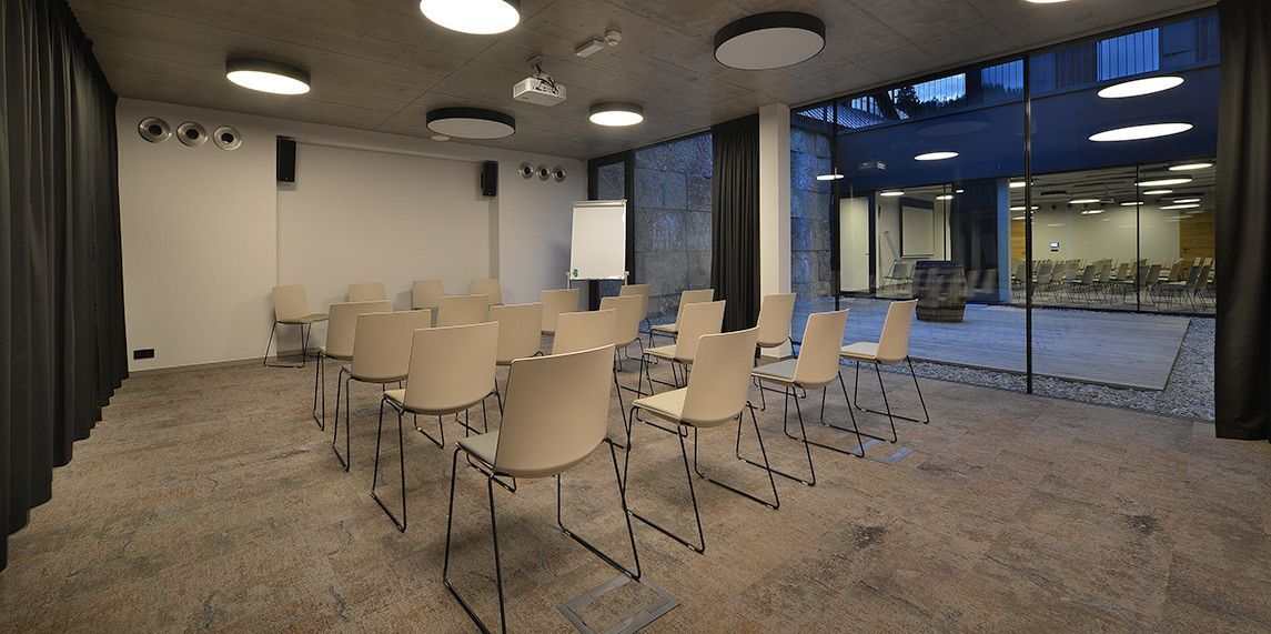 Konferenční místnost se stoly a židlemi a velkým oknem.