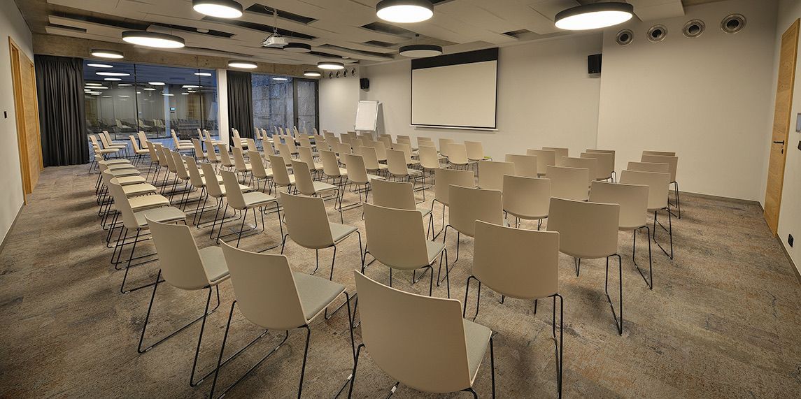 Velká konferenční místnost s řadami židlí a promítacím plátnem.