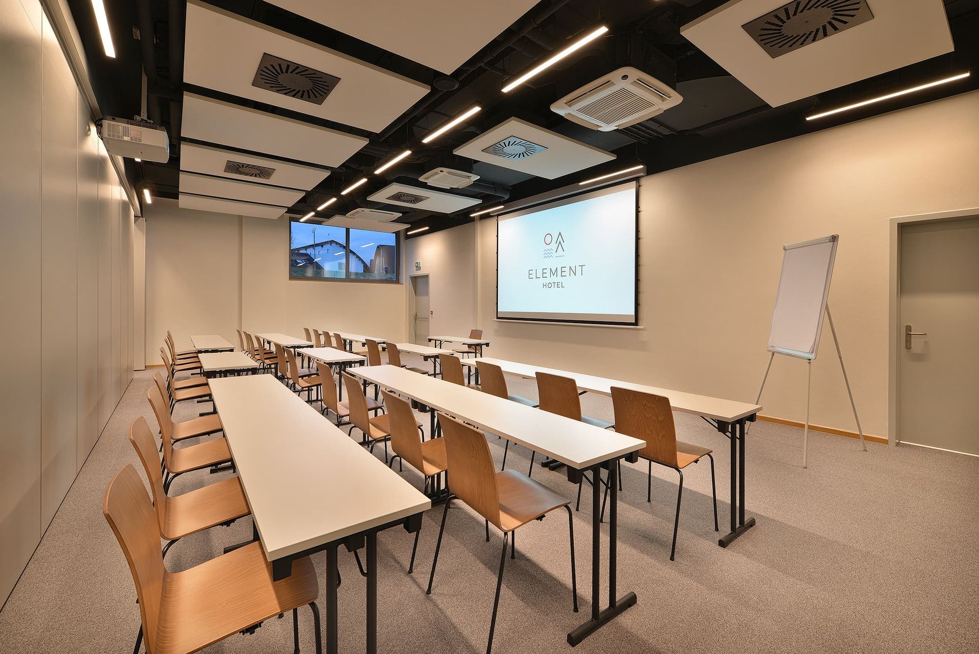 Velká konferenční místnost se stoly a židlemi a promítacím plátnem.