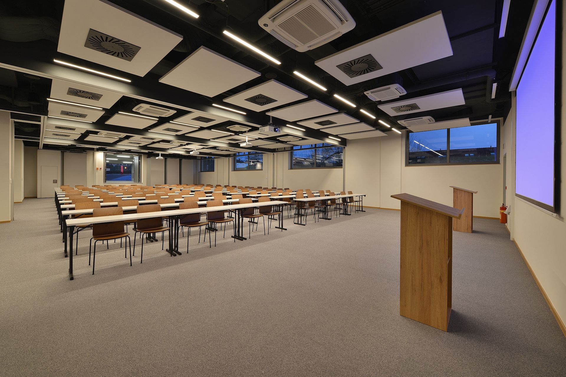 Velká konferenční místnost se stoly a židlemi a pódium.