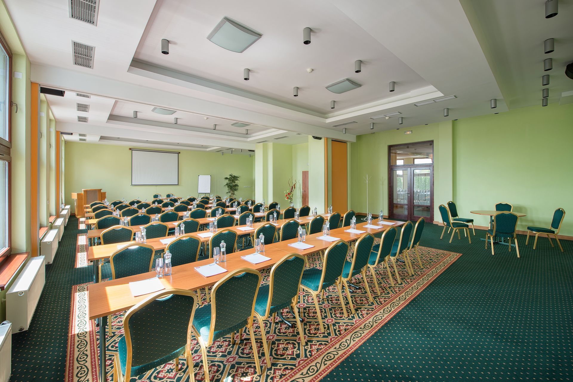 Velká konferenční místnost se stoly a židlemi a promítacím plátnem.