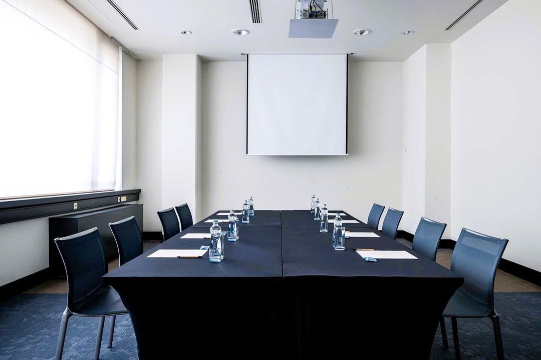 Konferenční místnost s dlouhým stolem a židlemi a TV s plochou obrazovkou.