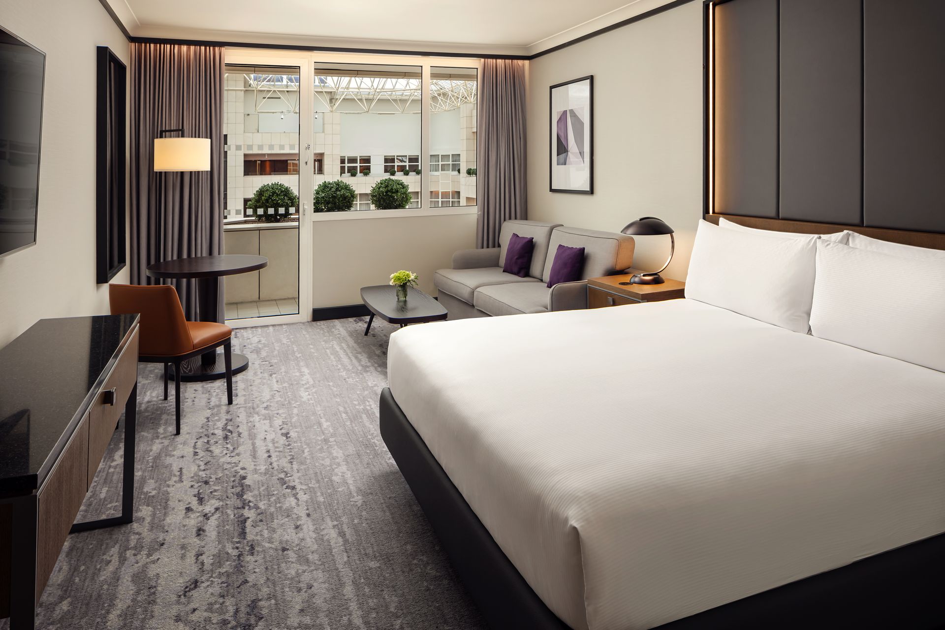 Hotelový pokoj s manželskou postelí , židlí , stolem a zrcadlem.