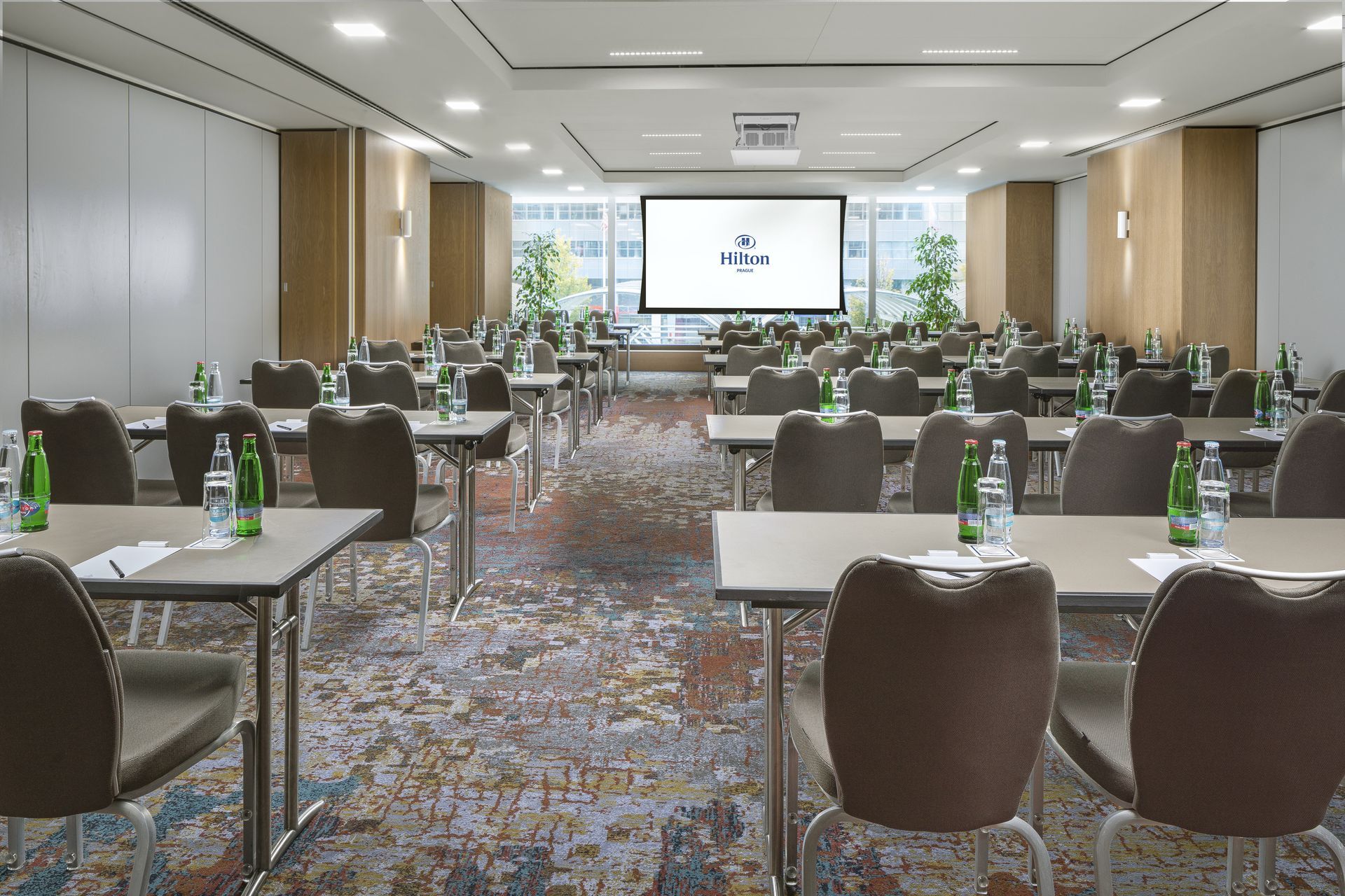 Velká konferenční místnost se stoly a židlemi a projektorem.