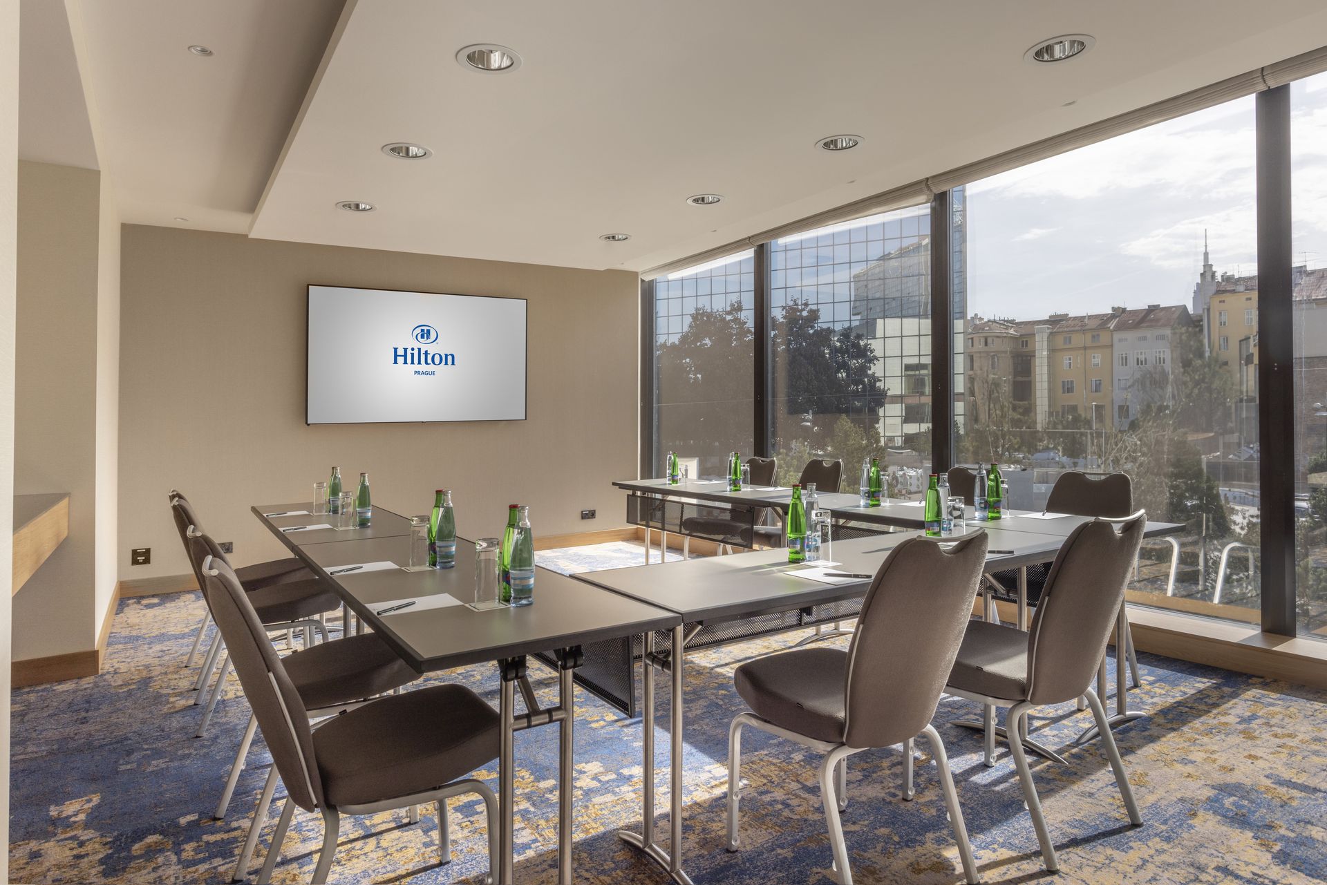 Restaurace se stoly a židlemi před velkoplošnou obrazovkou.