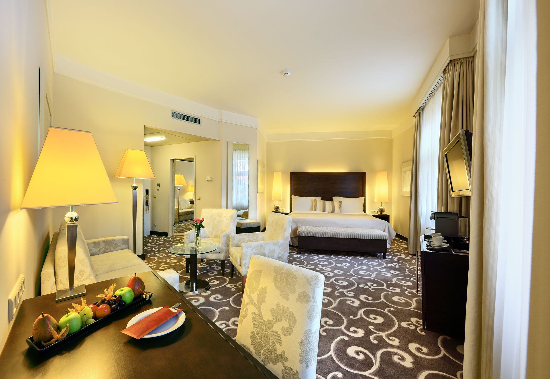 Hotelový pokoj s manželskou postelí a stolem s ovocem na ní.