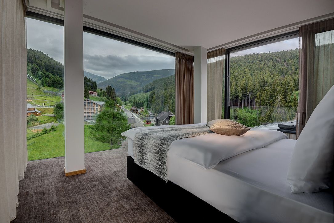 Ložnice s postelí a velkým oknem s výhledem na hory.