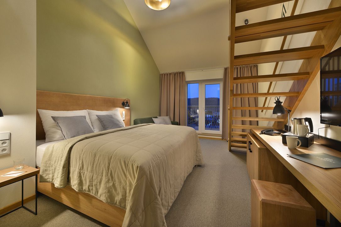 Hotelový pokoj s manželskou postelí , stolem , židlí a schody.