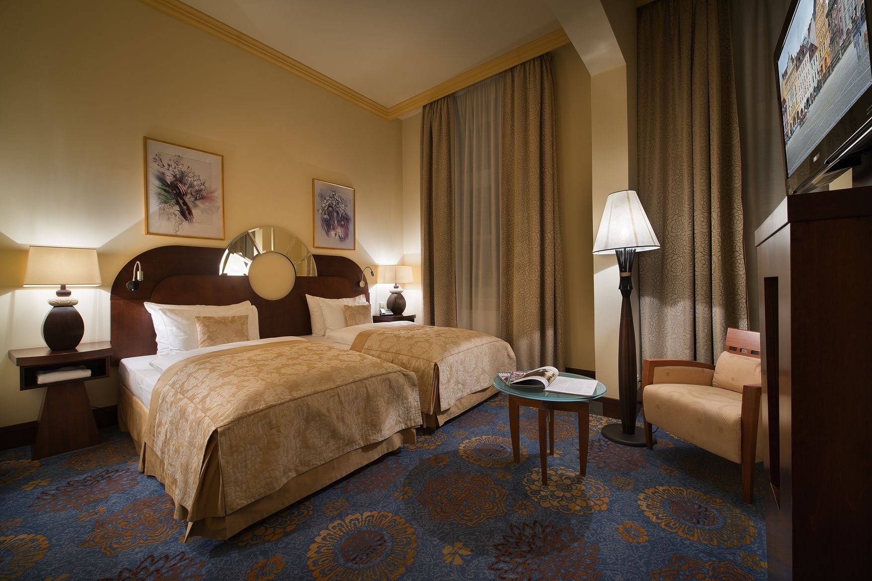 Hotelový pokoj se dvěma lůžky, židlí, stolem a televizí.