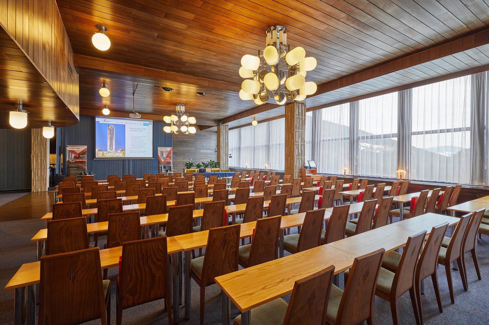 Velká místnost se stoly a židlemi a promítacím plátnem.