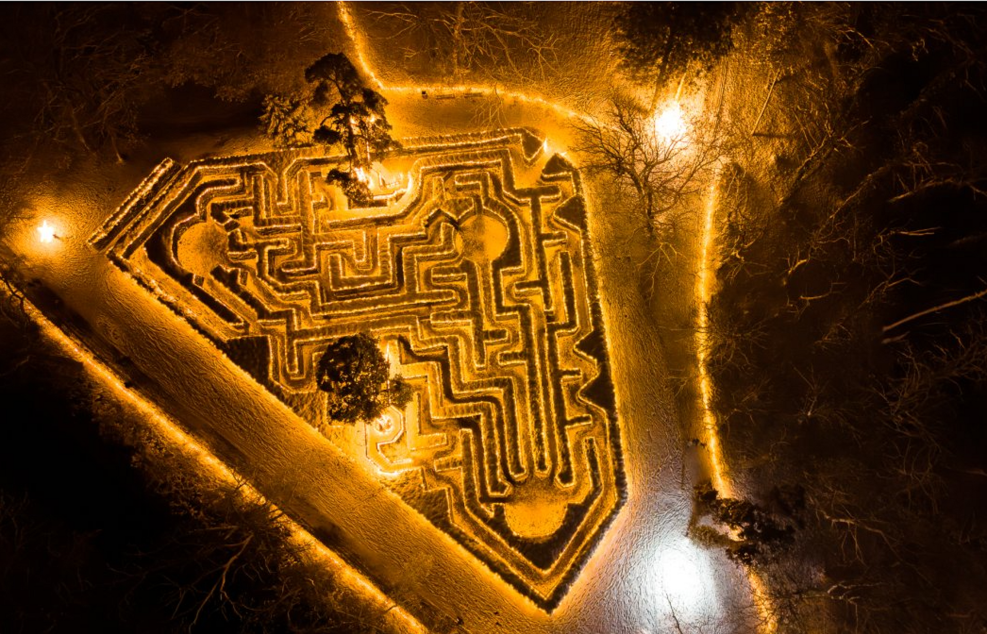 Velké bludiště ze živého plotu v parku se sluncem prosvítajícím mezi stromy.