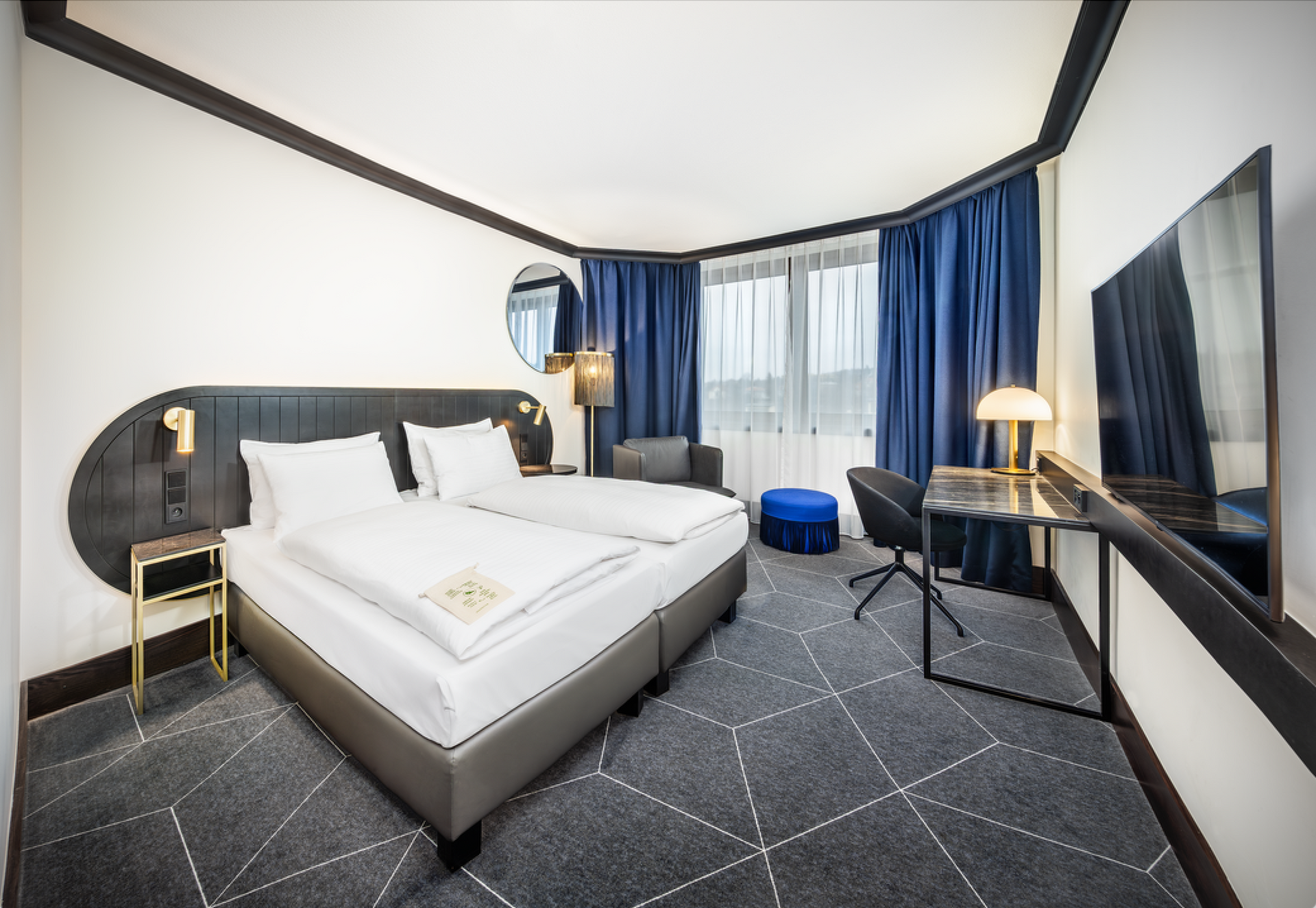 Hotelový pokoj s manželskou postelí , židlí , stolem a zrcadlem.