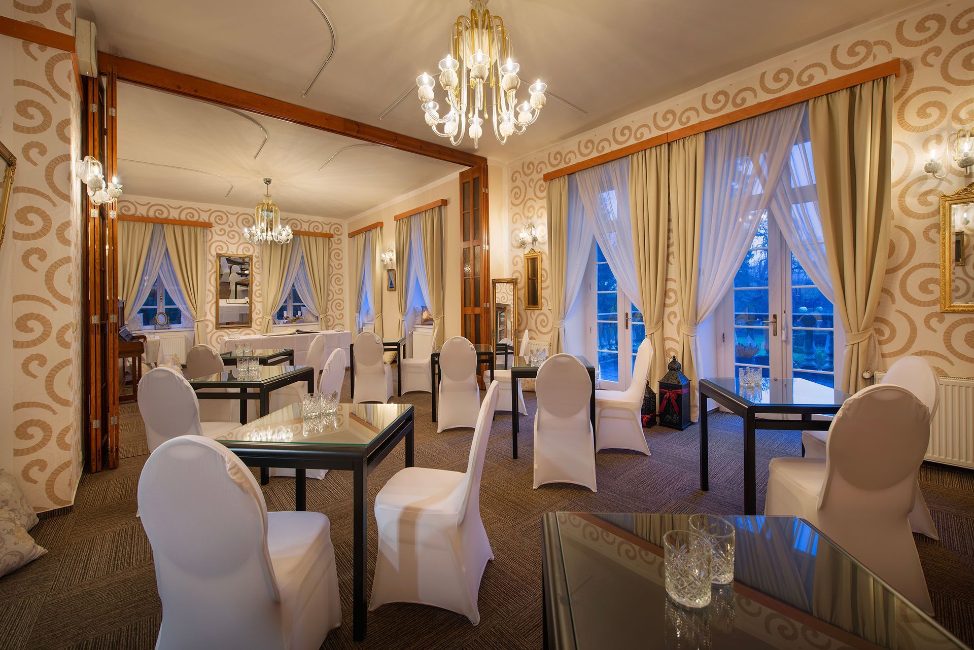 Velká místnost se stoly a židlemi a lustrem.