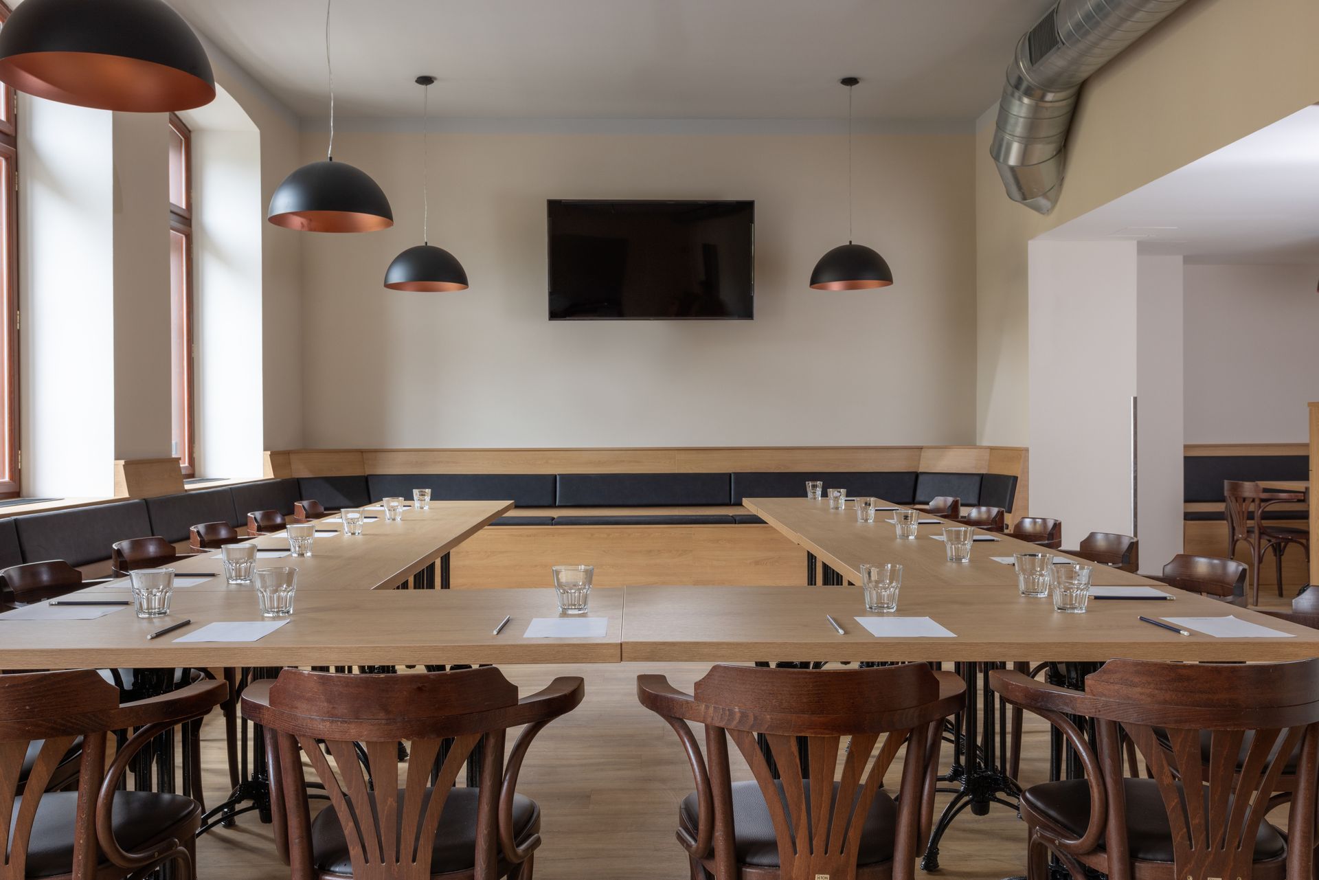 Velký pokoj se stoly a židlemi a TV s plochou obrazovkou na zdi.