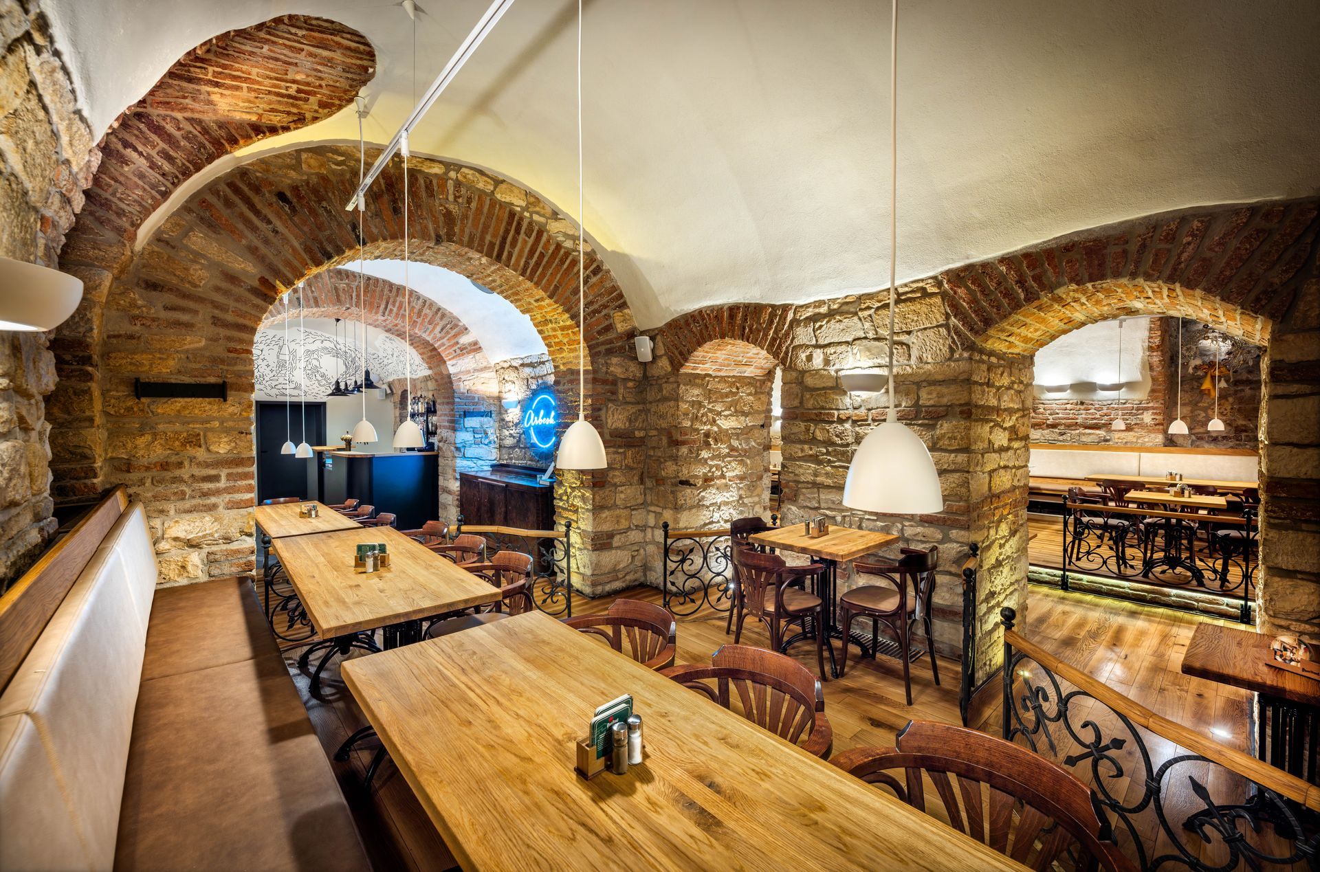 Restaurace s dřevěnými stoly a židlemi a kamennou zdí.