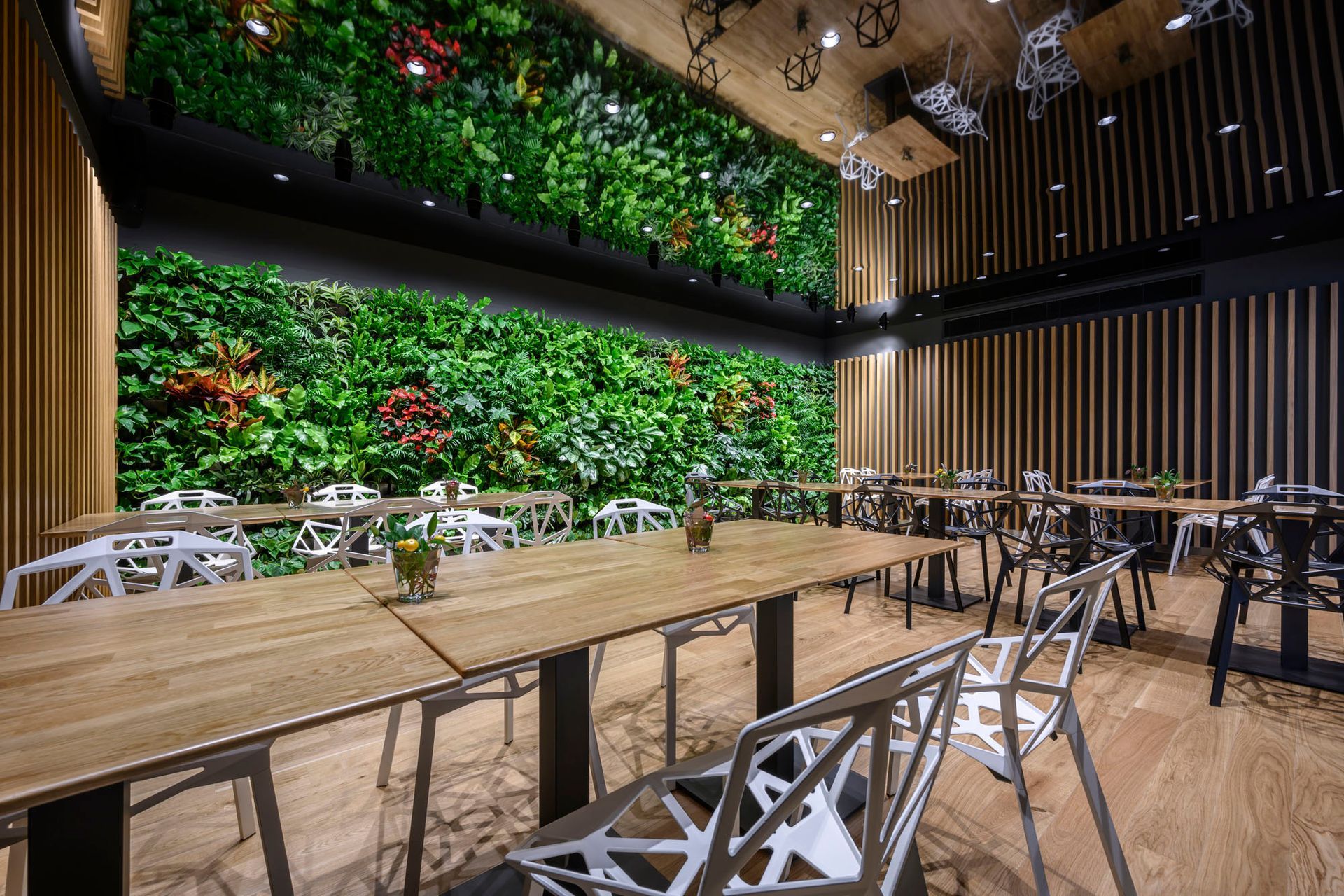 Restaurace se stoly a židlemi a zelenou stěnou.