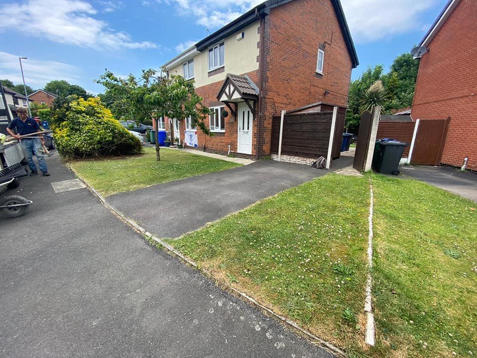A two-story brick and cream home with a front driveway, green lawn, and a person standing near the street.