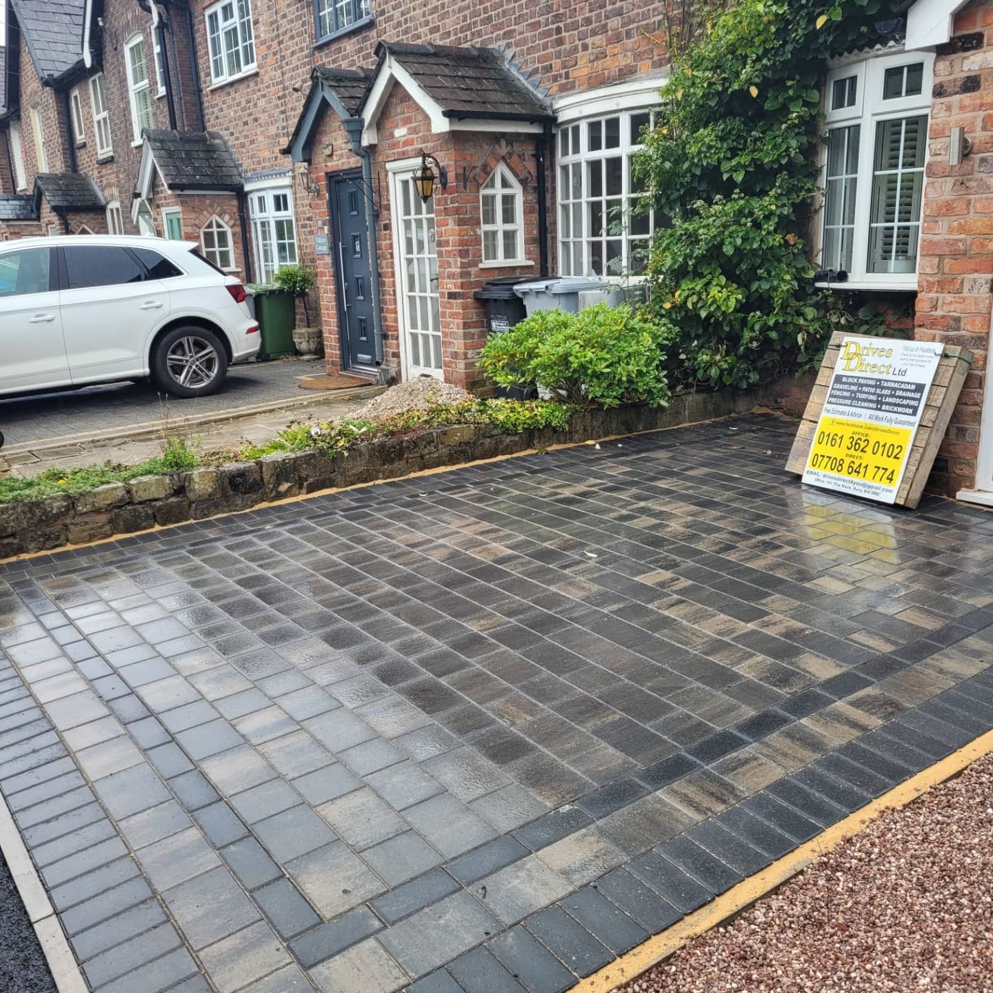 A freshly laid gray block-paving driveway in front of a brick house with a white car parked to the left.