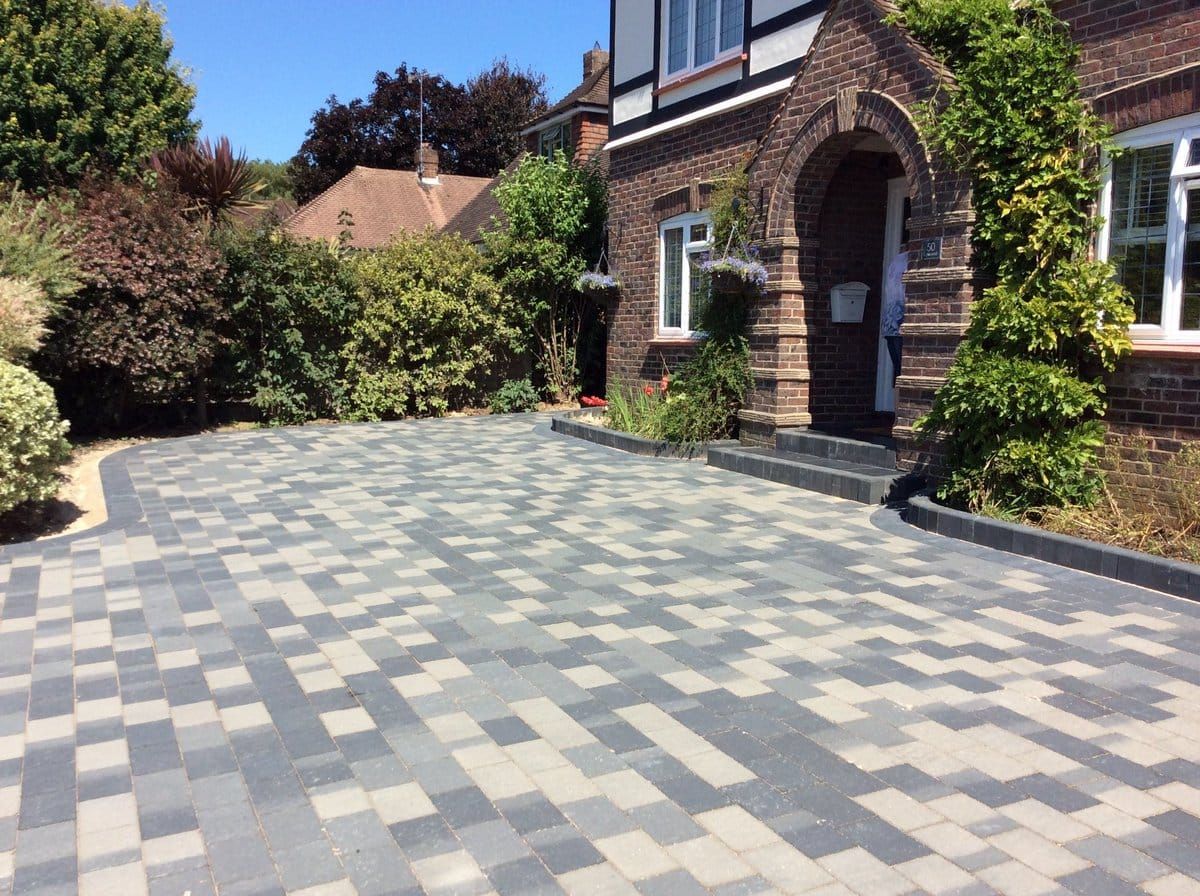 A modern paved driveway with a blend of grey and white rectangular bricks leading to a brick house with an arched entry.