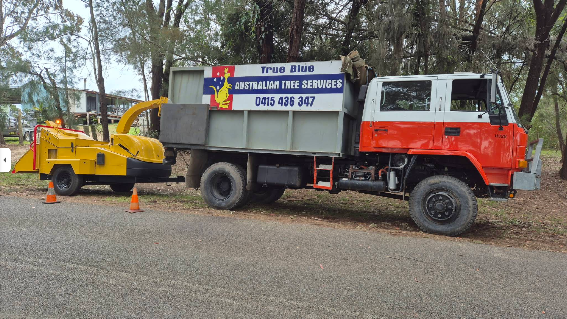 Tow truck with crane and sign parked roadside beside orange traffic cones and a small excavator — True Blue Australian Tree Services in Morisset, NSW