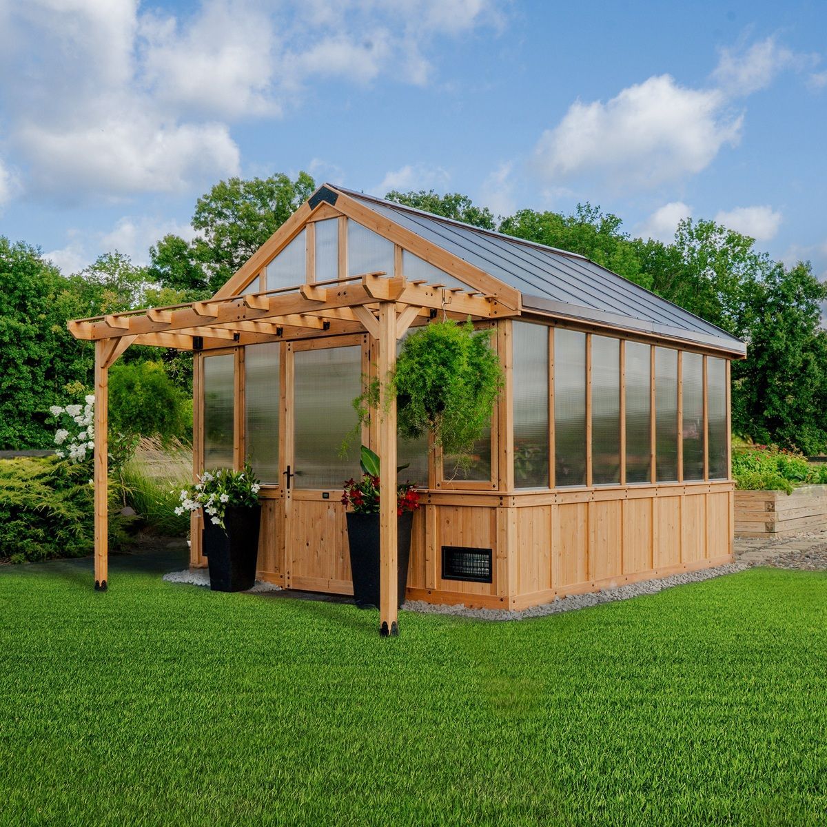 Wooden greenhouse with glass panels and a pergola on a green lawn under a blue sky
