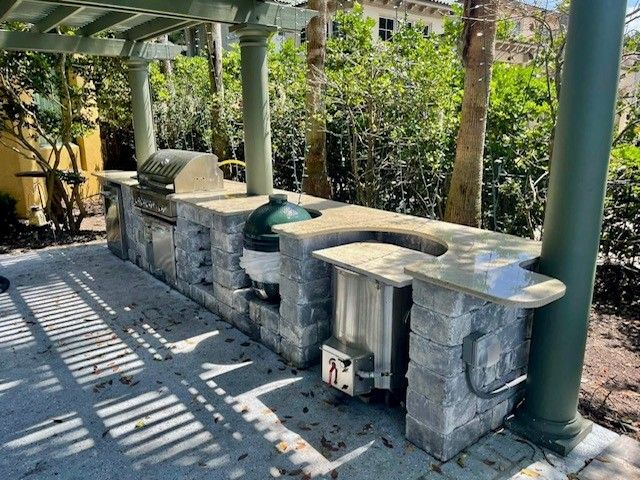 Outdoor stone barbecue station with green columns and slatted sunlight under a pergola