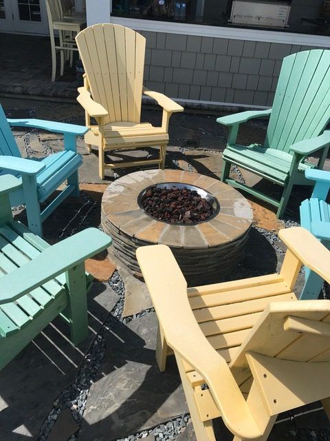 Colorful Adirondack chairs around a round fire pit on a sunny patio.