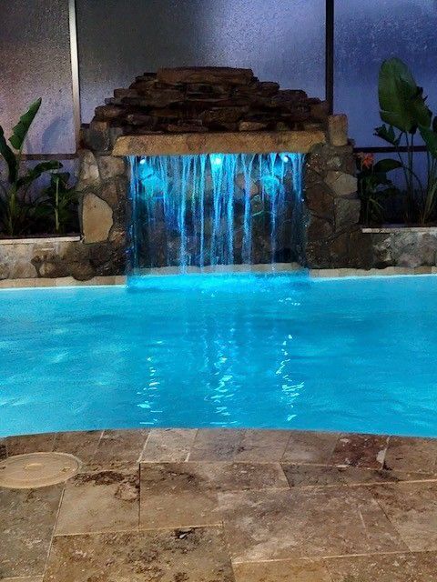 Blue pool with a small waterfall fountain and stone ledge at night