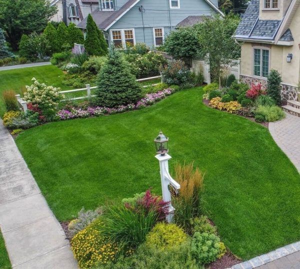 Manicured green lawn in a suburban front yard with flower beds, shrubs, and a walkway by the house