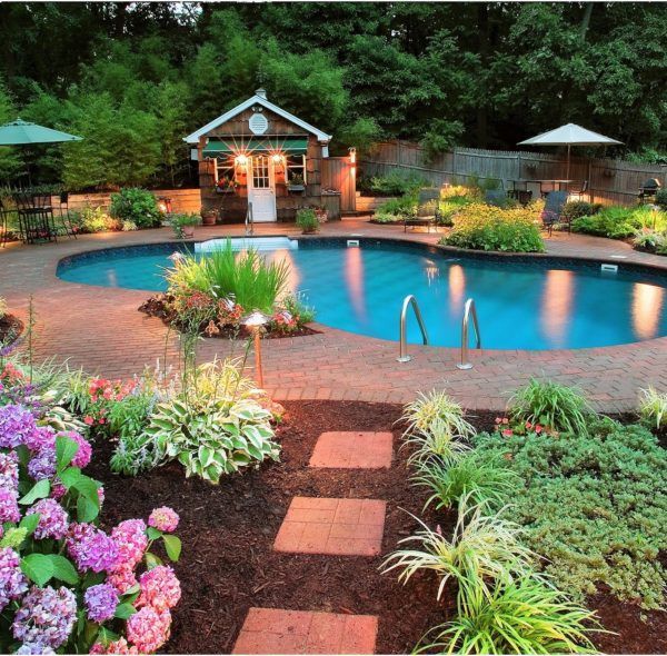 Lush backyard pool with a small pavilion, stone path, and colorful flower beds at dusk