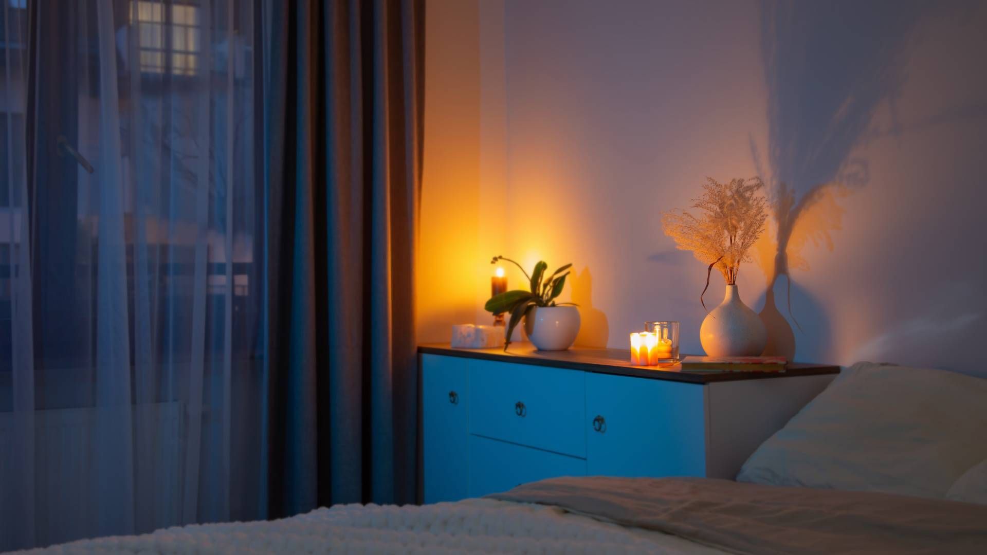 A bedroom at night with layered curtains and lit candles on a white dresser at Exciting Windows! by 