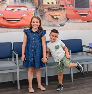 Girl and boy holding hands, smiling, in front of Cars movie poster, in waiting room.