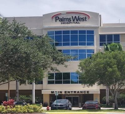 Palms West Hospital building with main entrance, blue windows, and parked cars.